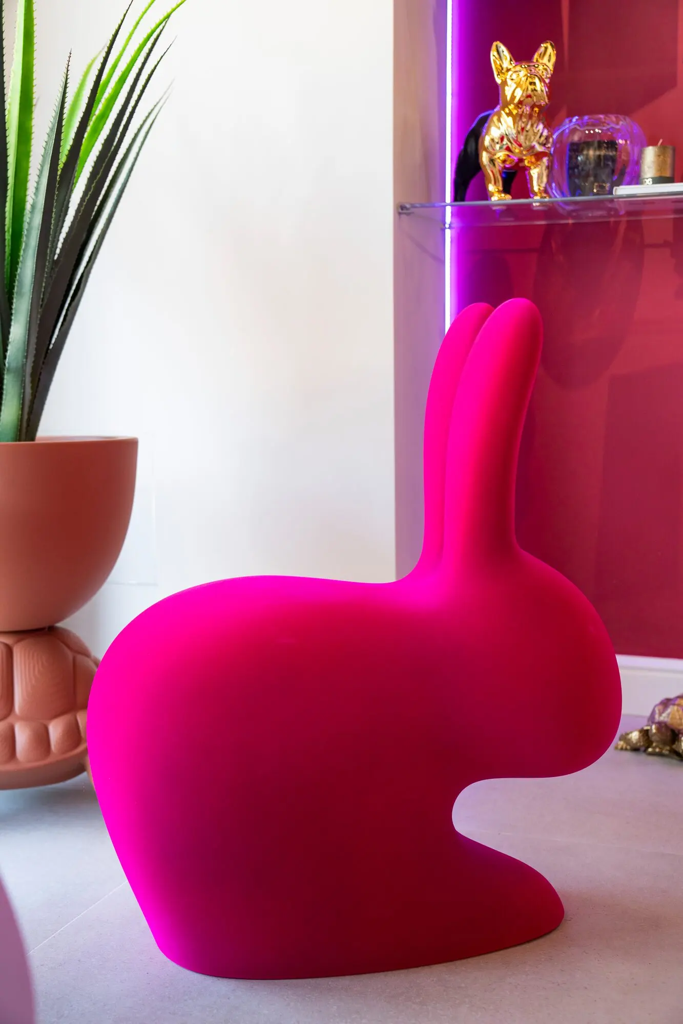 Sedia a forma di coniglio in velluto fucsia davanti a una parete bordeaux.