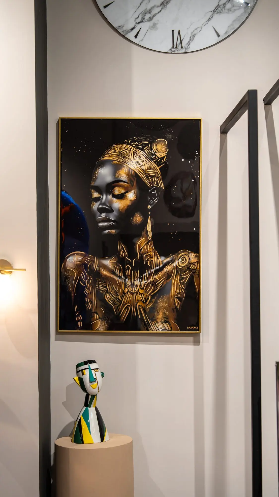 Quadro con il ritratto di una donna con decorazioni dorate, accanto a un orologio da parete e a una scultura colorata.
